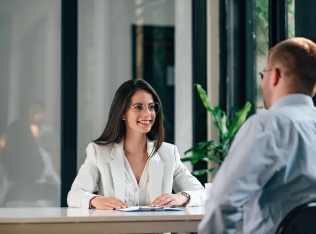 a woman in a white suit sitting at a table with a man in a suit